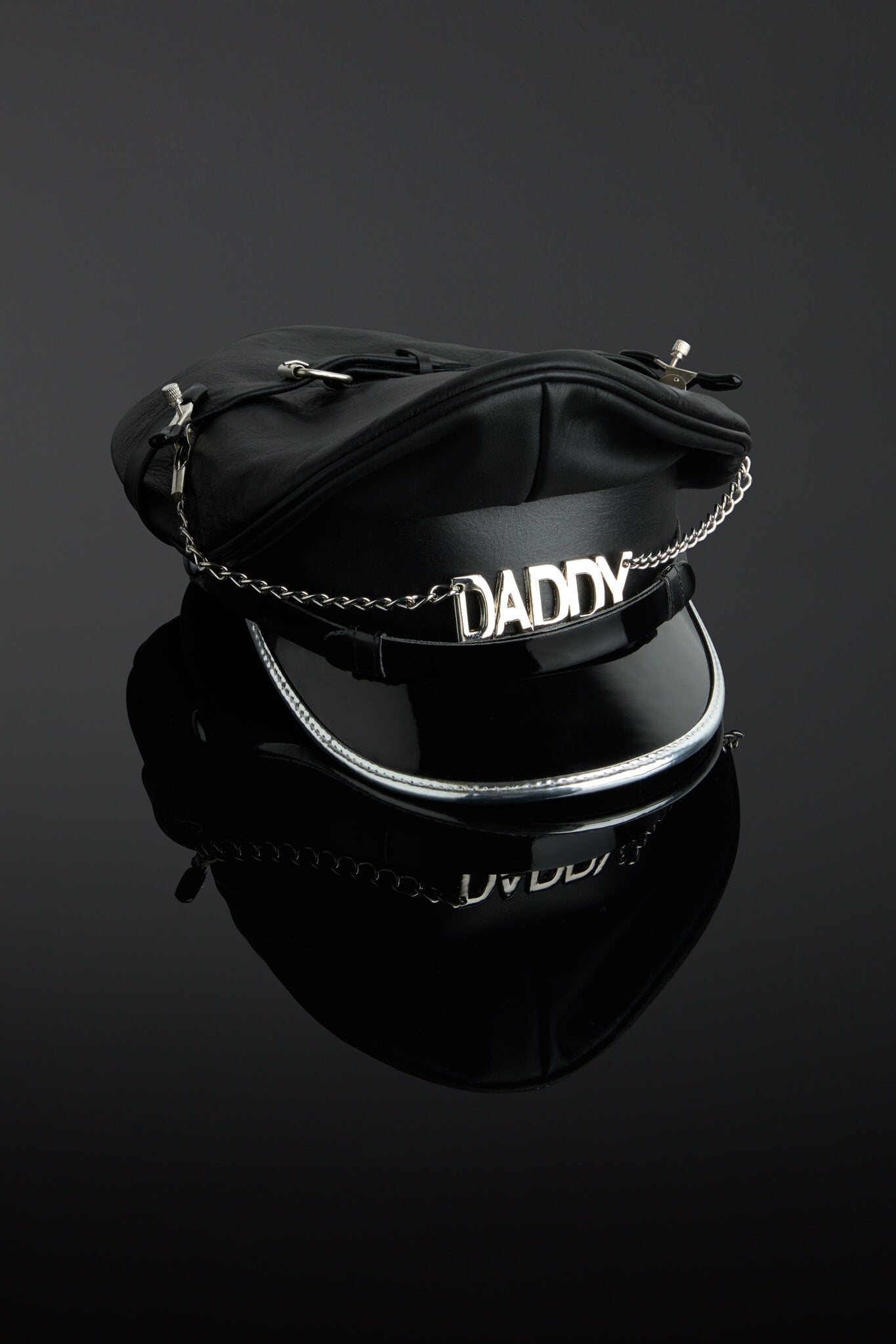 Black leather helmet with 'DADDY' chain on a reflective black surface