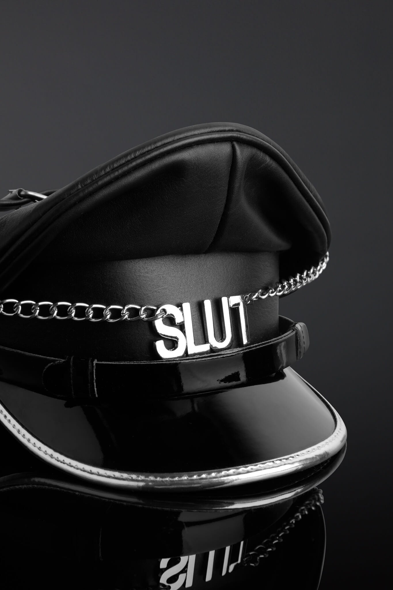 Black police hat with 'SLUT' chain on a reflective surface against a dark background