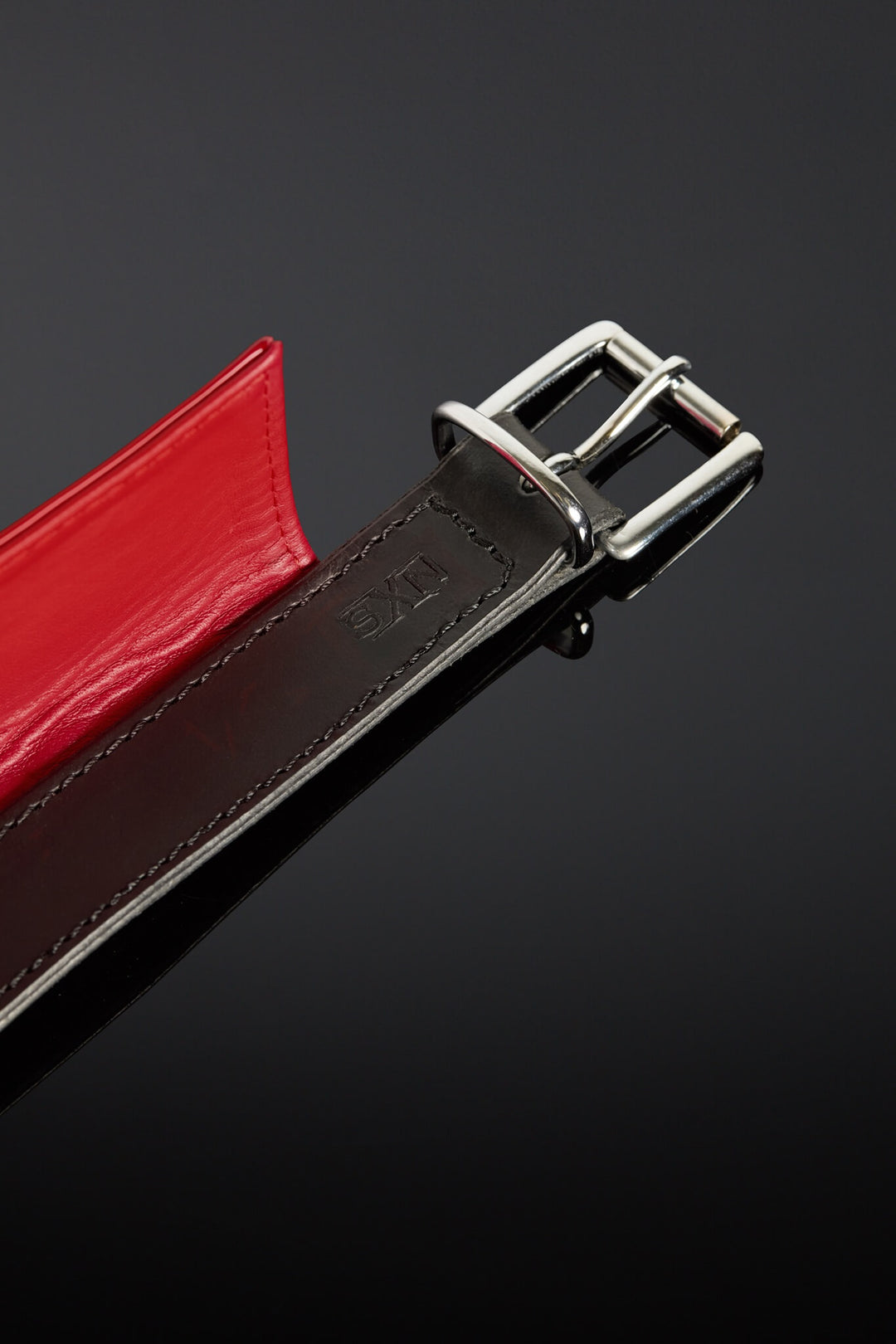 Close-up of a red and black leather belt with a silver buckle on a dark background