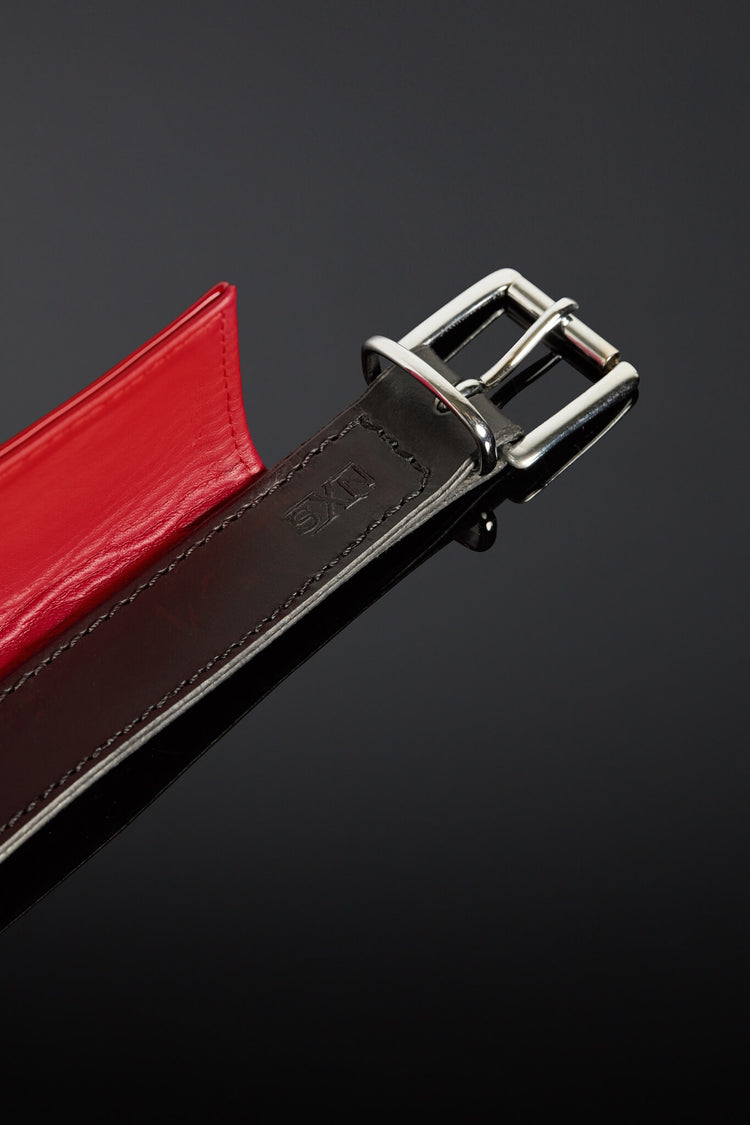 Close-up of a red and black leather belt with a silver buckle on a dark background
