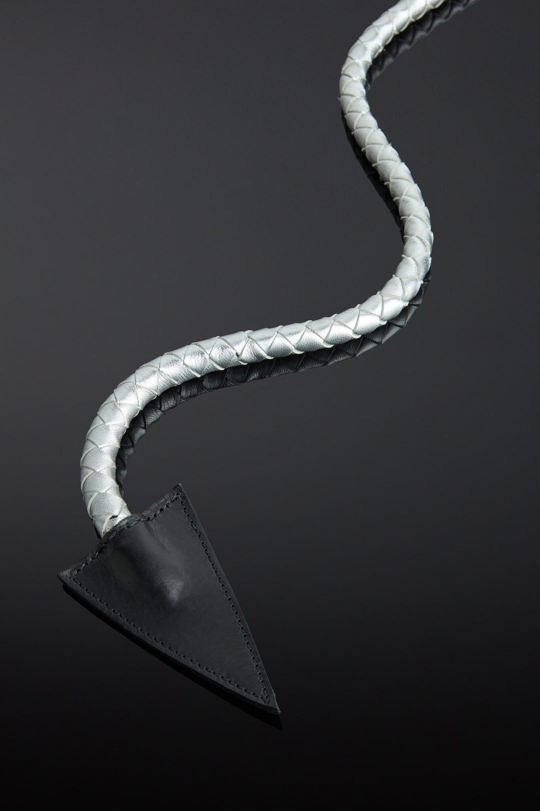 Metallic silver leather whip with a metal handle and pointed end on a reflective black surface - close up of whip end