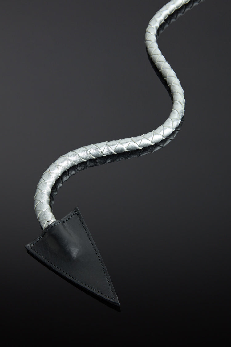 Metallic silver leather whip with a metal handle and pointed end on a reflective black surface - close up of whip end