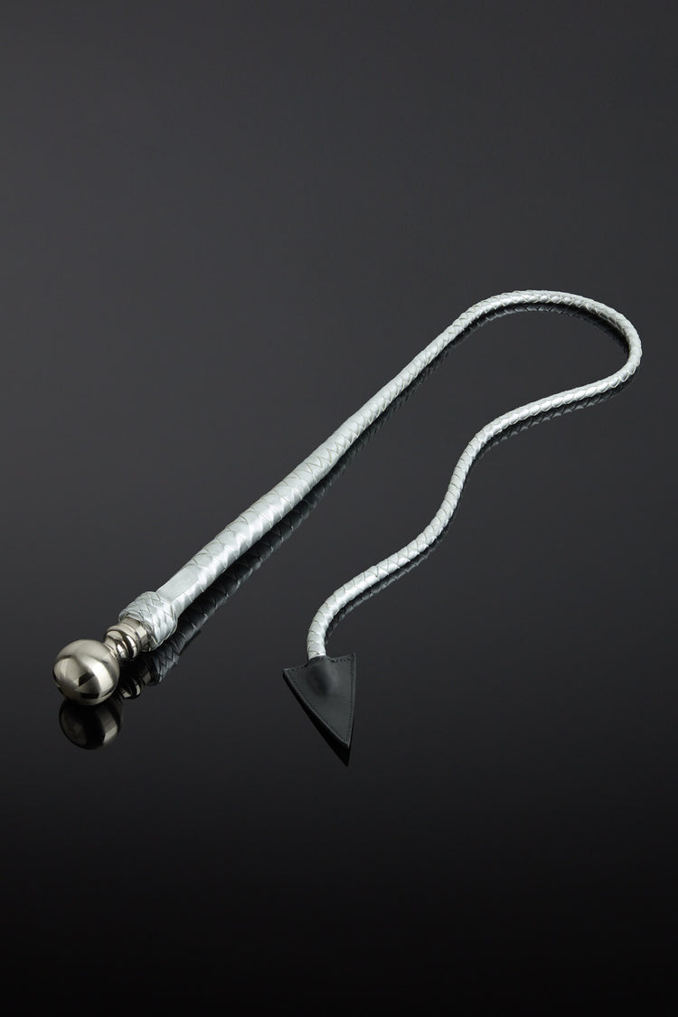 Metallic silver leather whip with a metal handle and pointed end on a reflective black surface