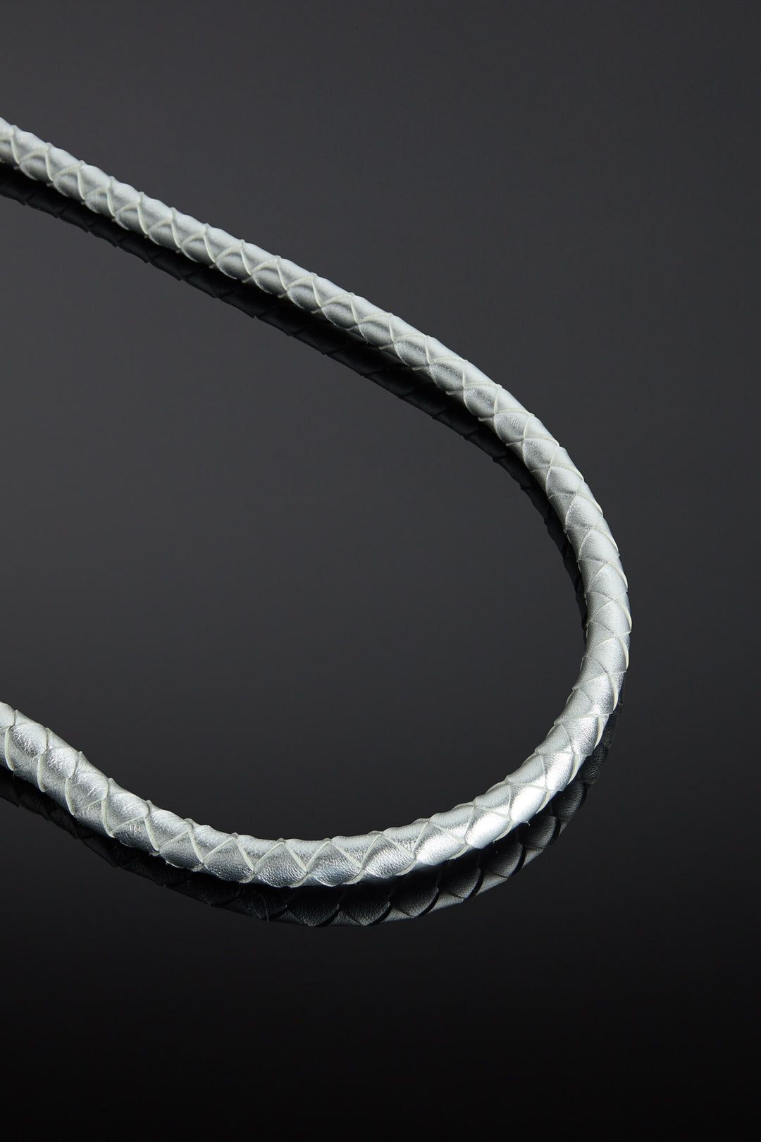 Close-up of a braided silver leather whip on a reflective black surface