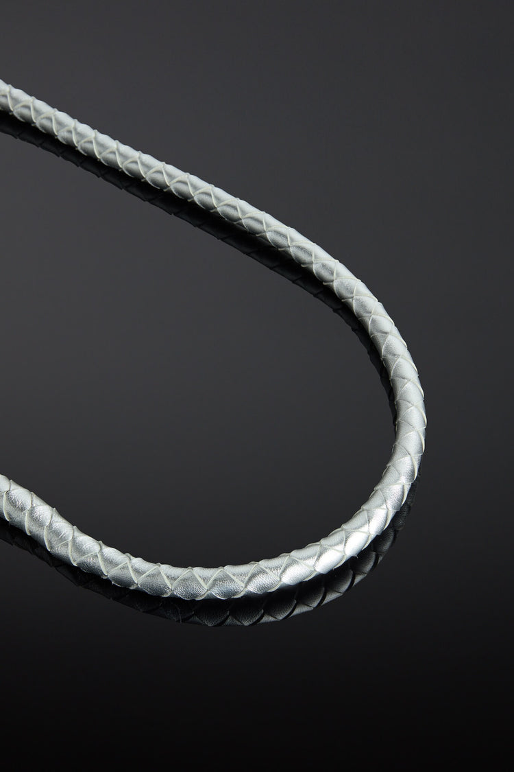 Close-up of a braided silver leather whip on a reflective black surface