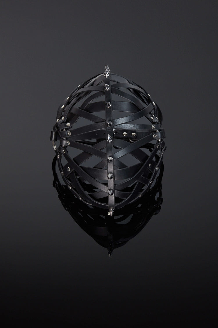 A black leather mask with metal spikes, featuring full grain leather straps woven in a symmetrical design.