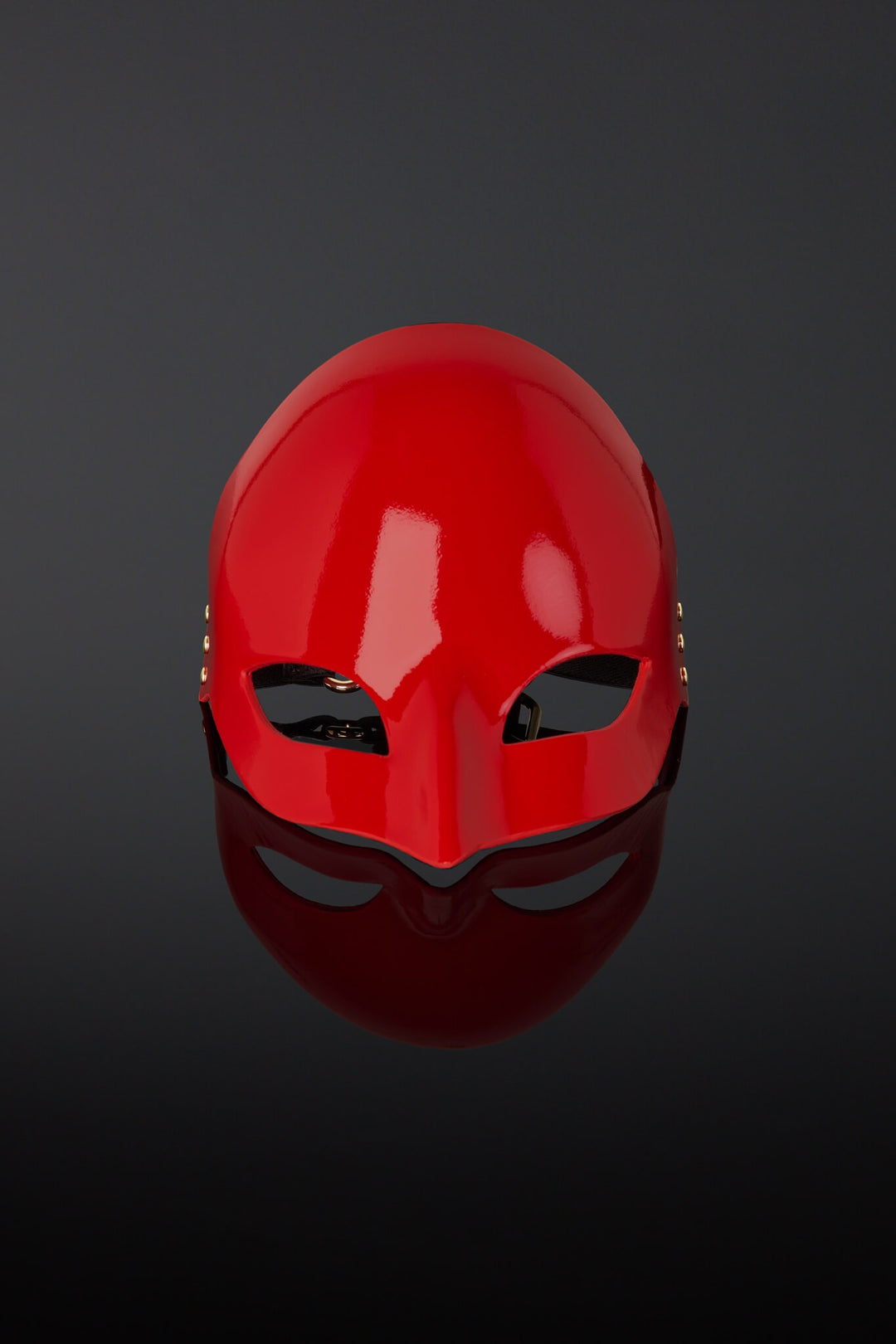 Red mask on a reflective black surface with a dark background