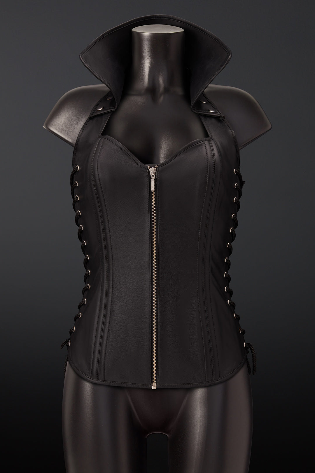 Black leather corset vest with shoulder armor and side lacing, displayed on a black mannequin torso against a dark gray background.