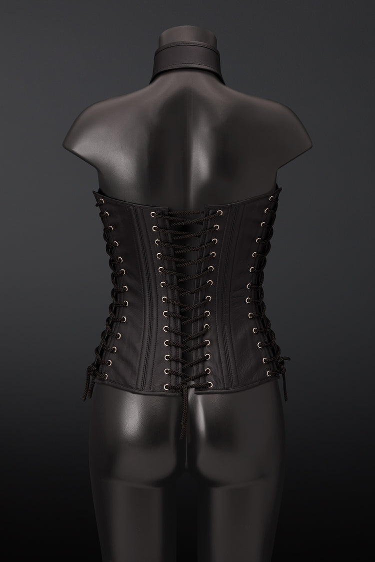 A black leather corset displayed on a black mannequin torso, viewed from the back. The corset features multiple rows of black laces threaded through brass eyelets.