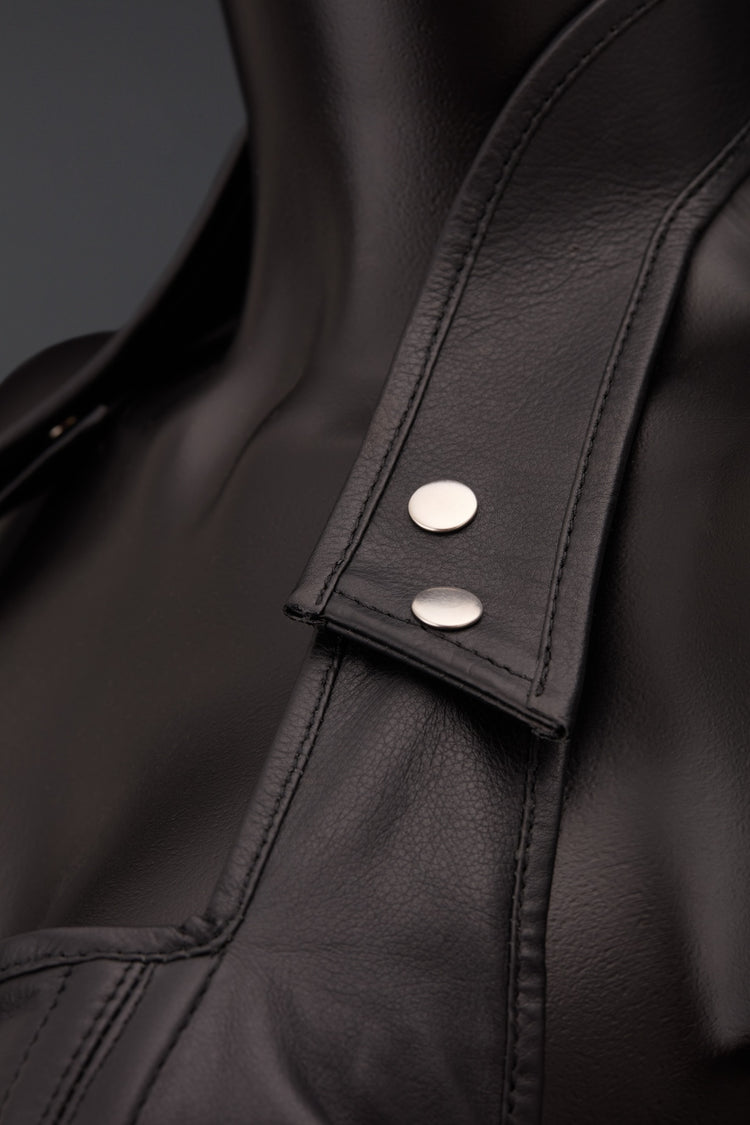 Close-up of a black leather corset featuring a pointed collar with two silver-tone snap buttons on a tab, set against a dark gray background.