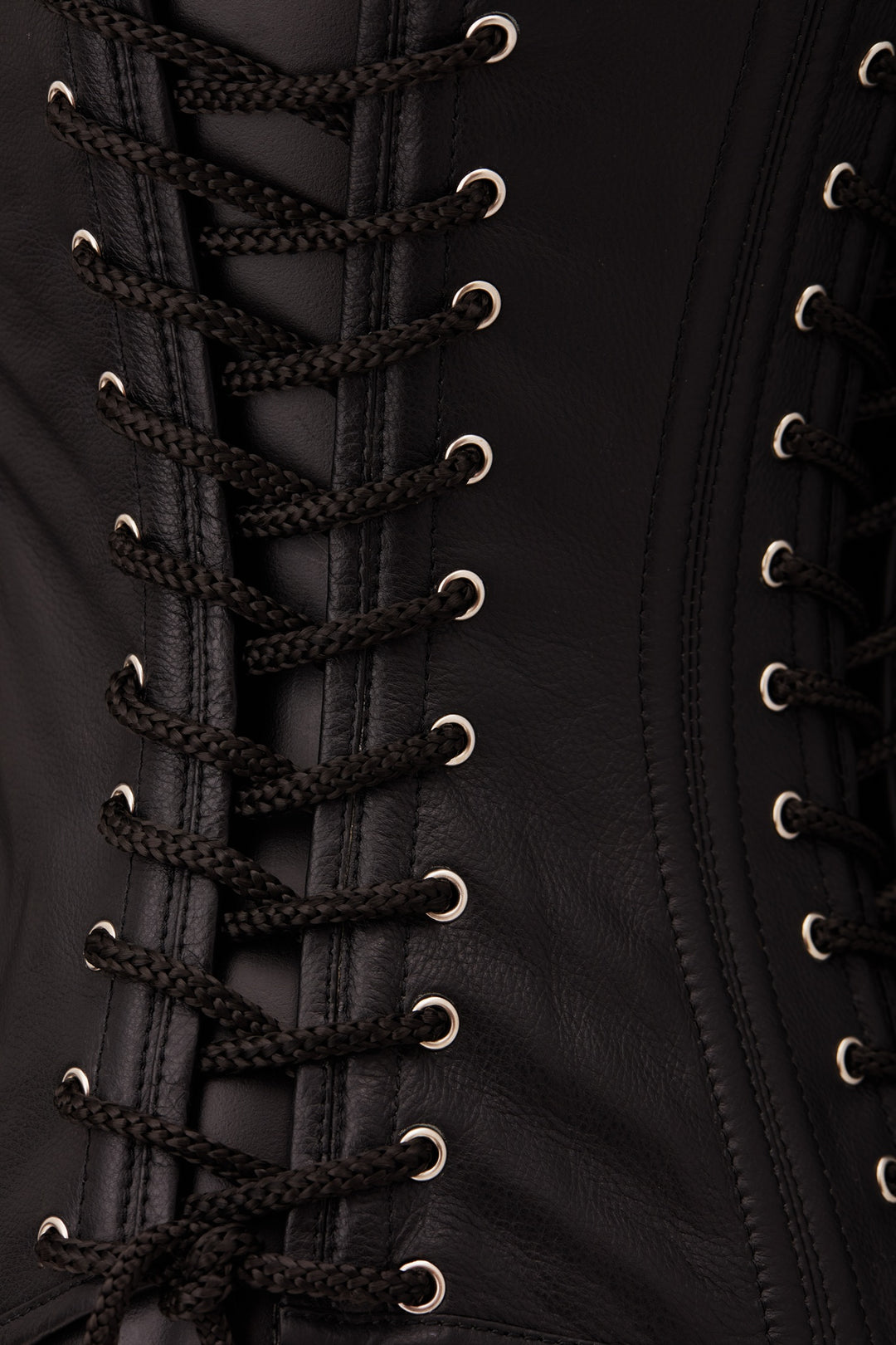 Close-up of a black leather corset with black braided laces threaded through silver metal eyelets.