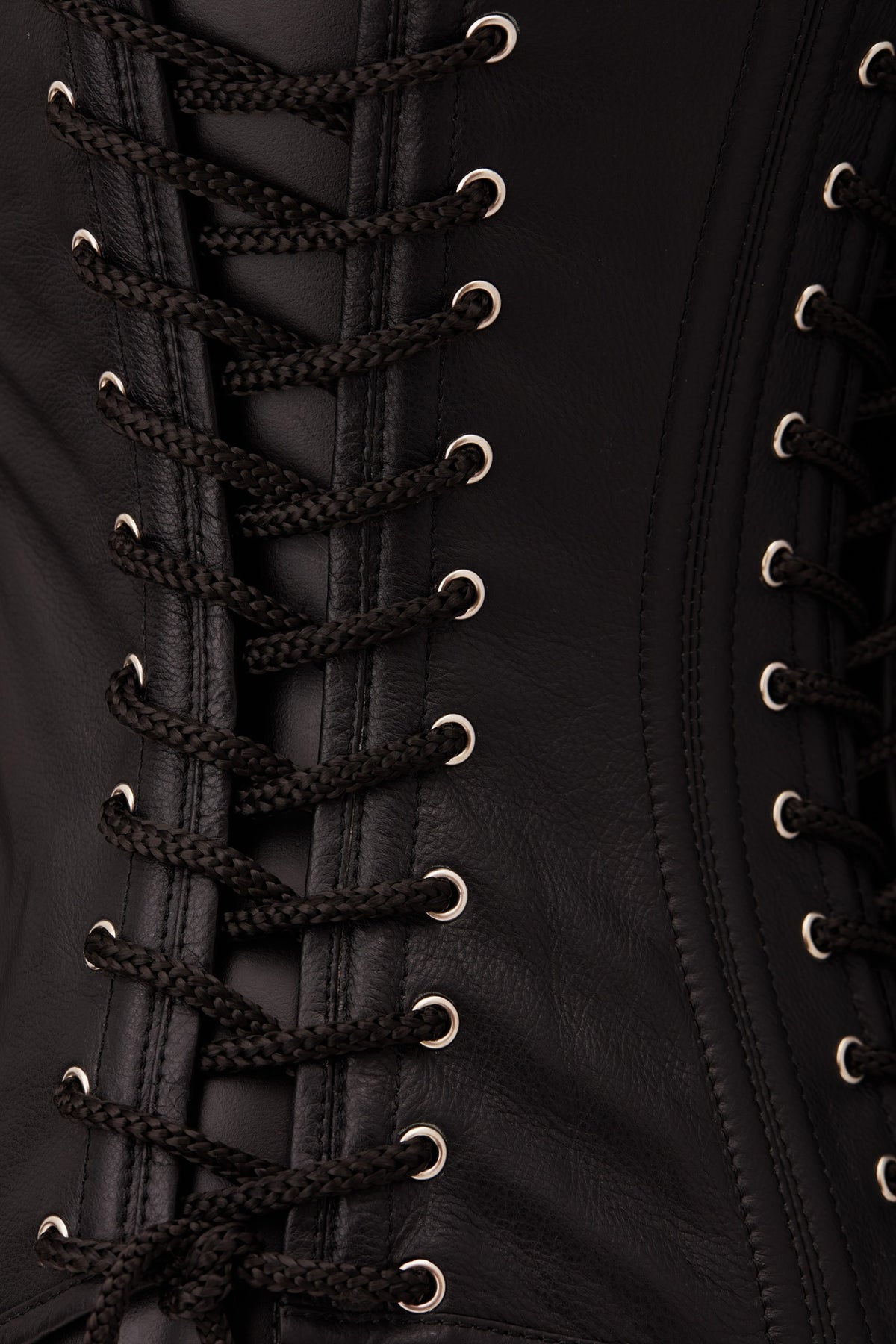 Close-up of a black leather corset with black braided laces threaded through silver metal eyelets.