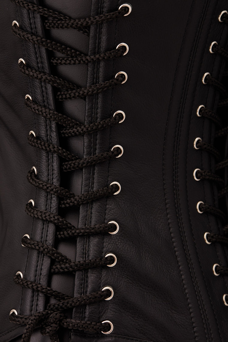 Close-up of a black leather corset with black braided laces threaded through silver metal eyelets.
