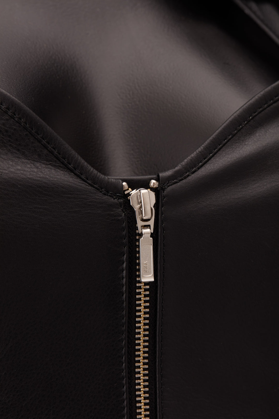 Close-up of a black leather zipper detail with a silver-toned pull tab on a black background.