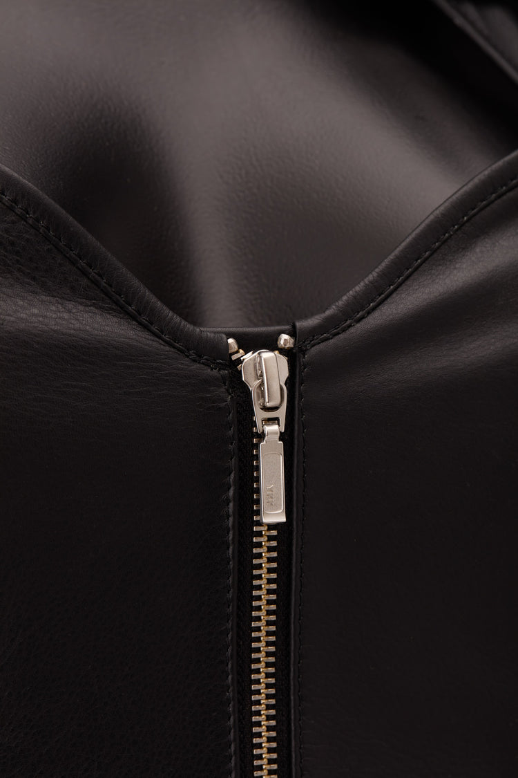 Close-up of a black leather zipper detail with a silver-toned pull tab on a black background.