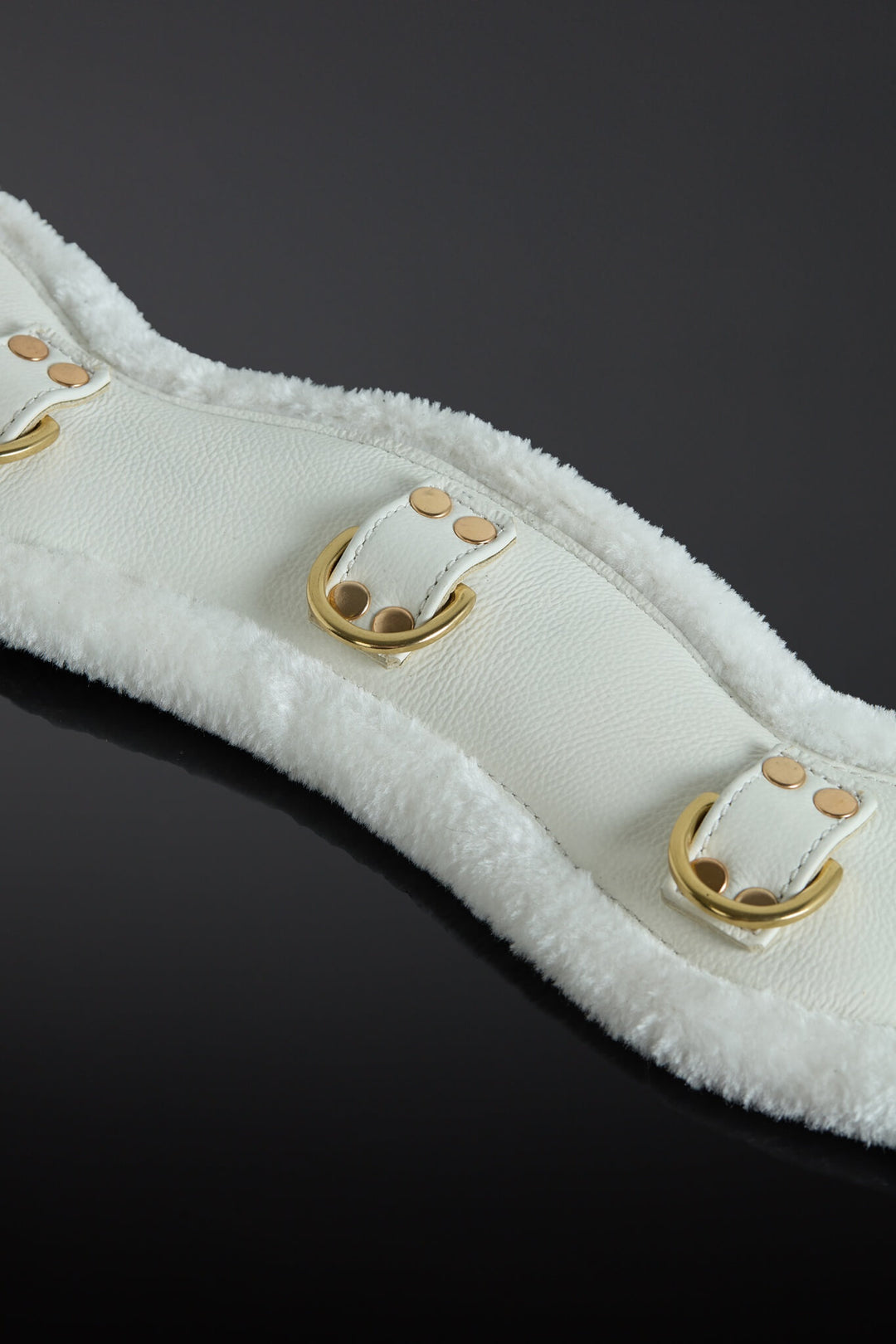 White leather strap with gold hardware on a black background