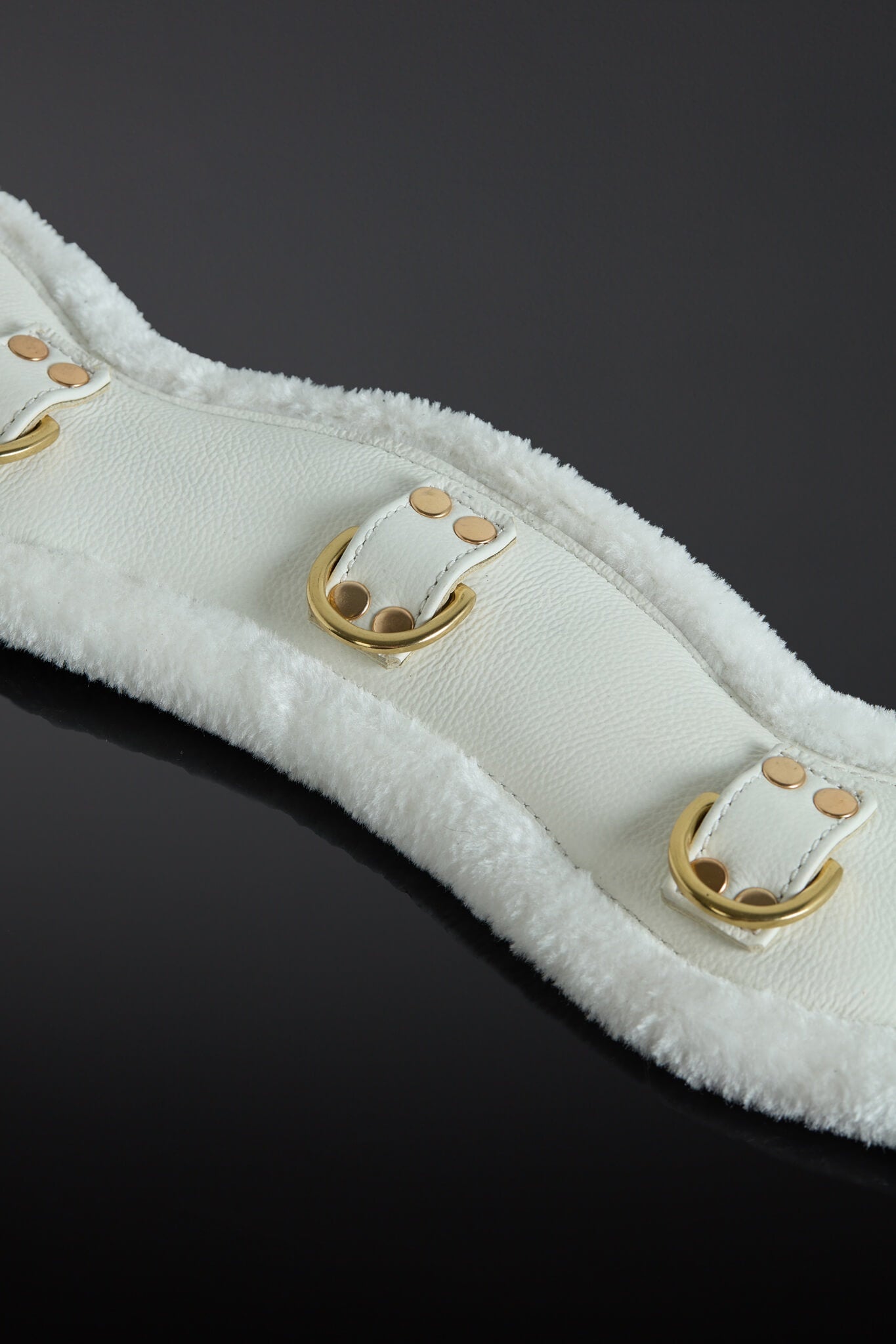 White leather strap with gold hardware on a black background