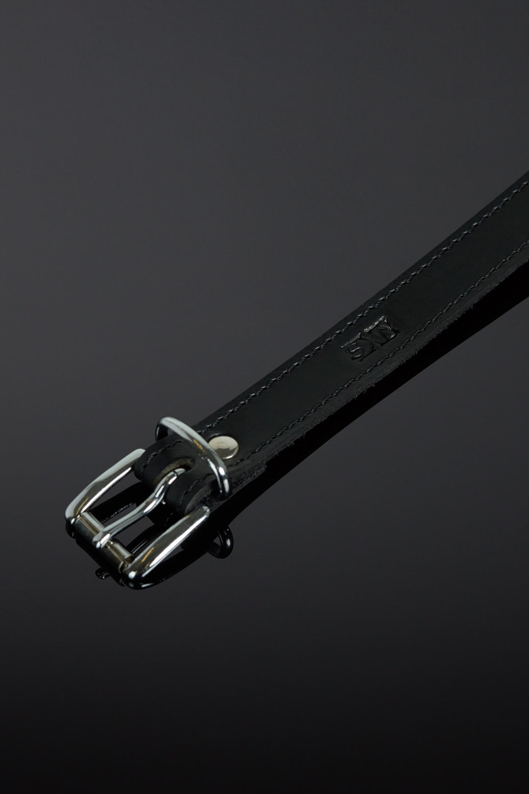 Black leather collar with silver buckle on a dark gray background