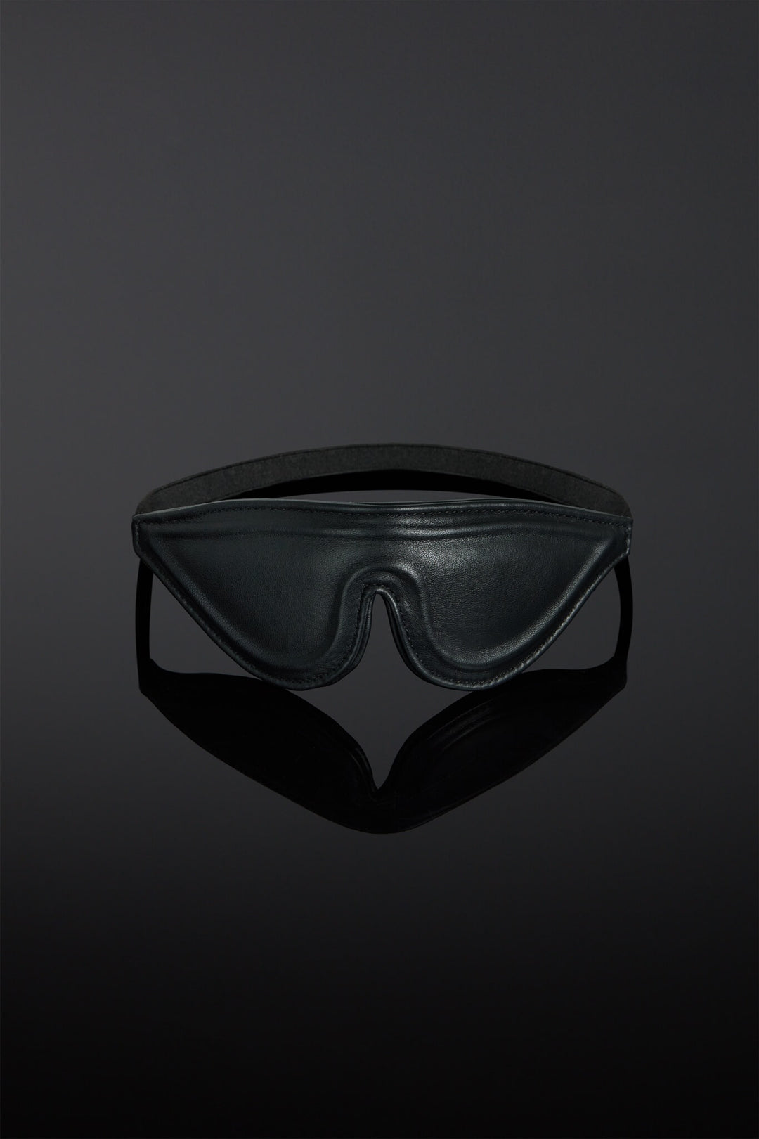 Black leather blindfold on a reflective black surface with a dark background