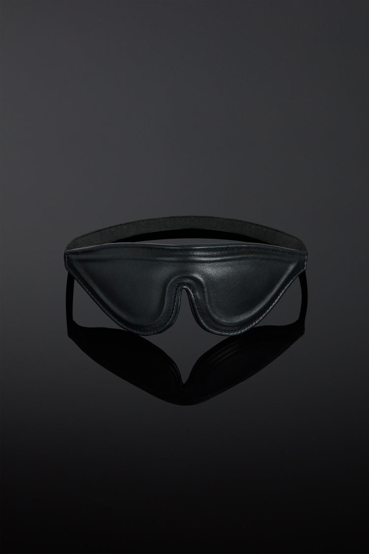 Black leather blindfold on a reflective black surface with a dark background