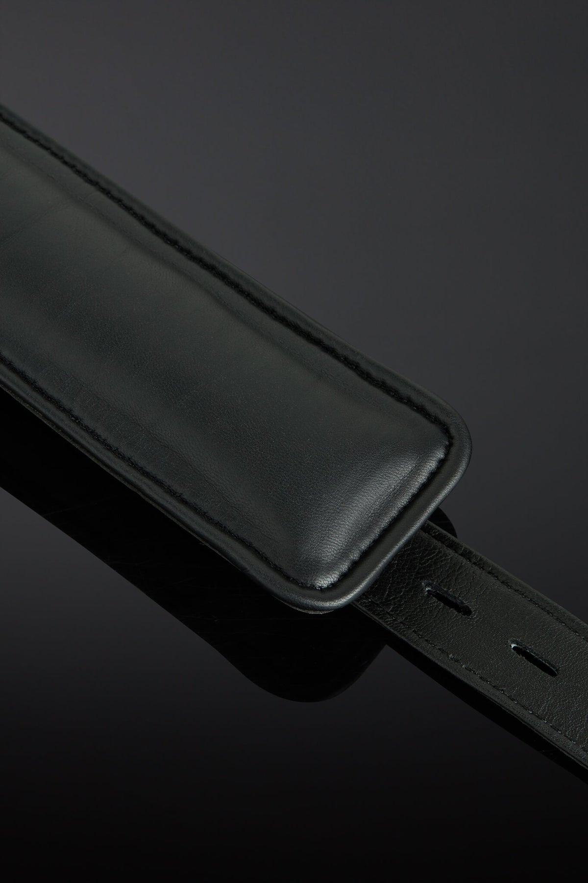 A close-up of a black leather interior cuffs with a matching black leather keeper or loop, photographed on a dark reflective background.
