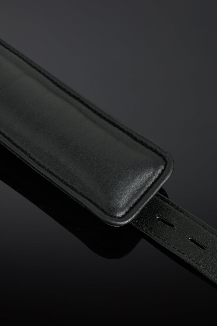 A close-up of a black leather interior cuffs with a matching black leather keeper or loop, photographed on a dark reflective background.