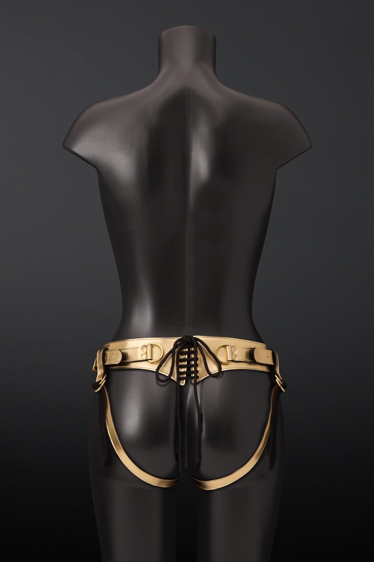 Picture showing gold leather strap on harness with brass color rivets on black mannequin with black background