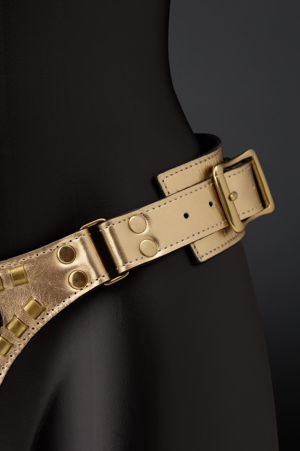 Picture showing gold leather strap on harness with brass color rivets on black mannequin with black background