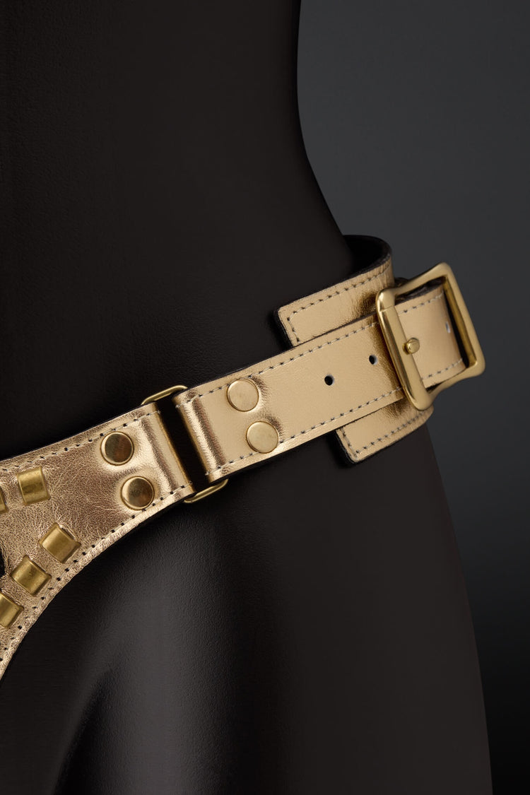Picture showing gold leather strap on harness with brass color rivets on black mannequin with black background