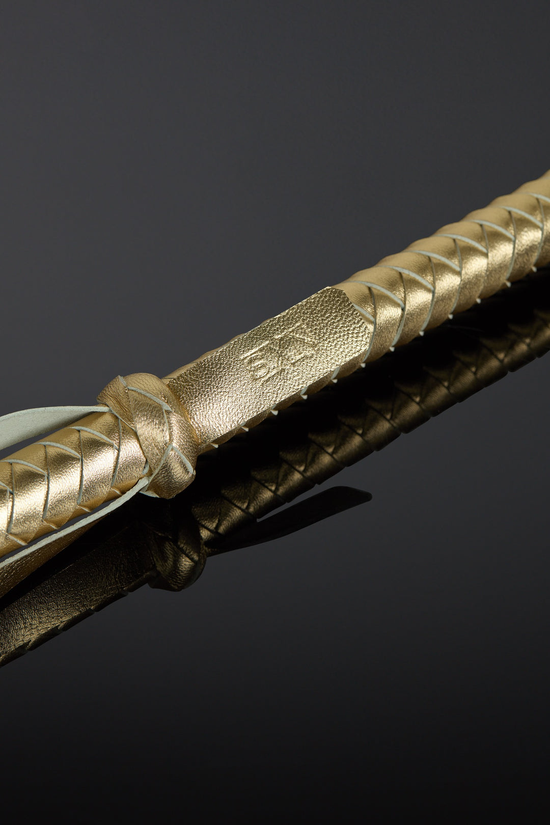 Close-up of a gold-handled leather baton on a black background