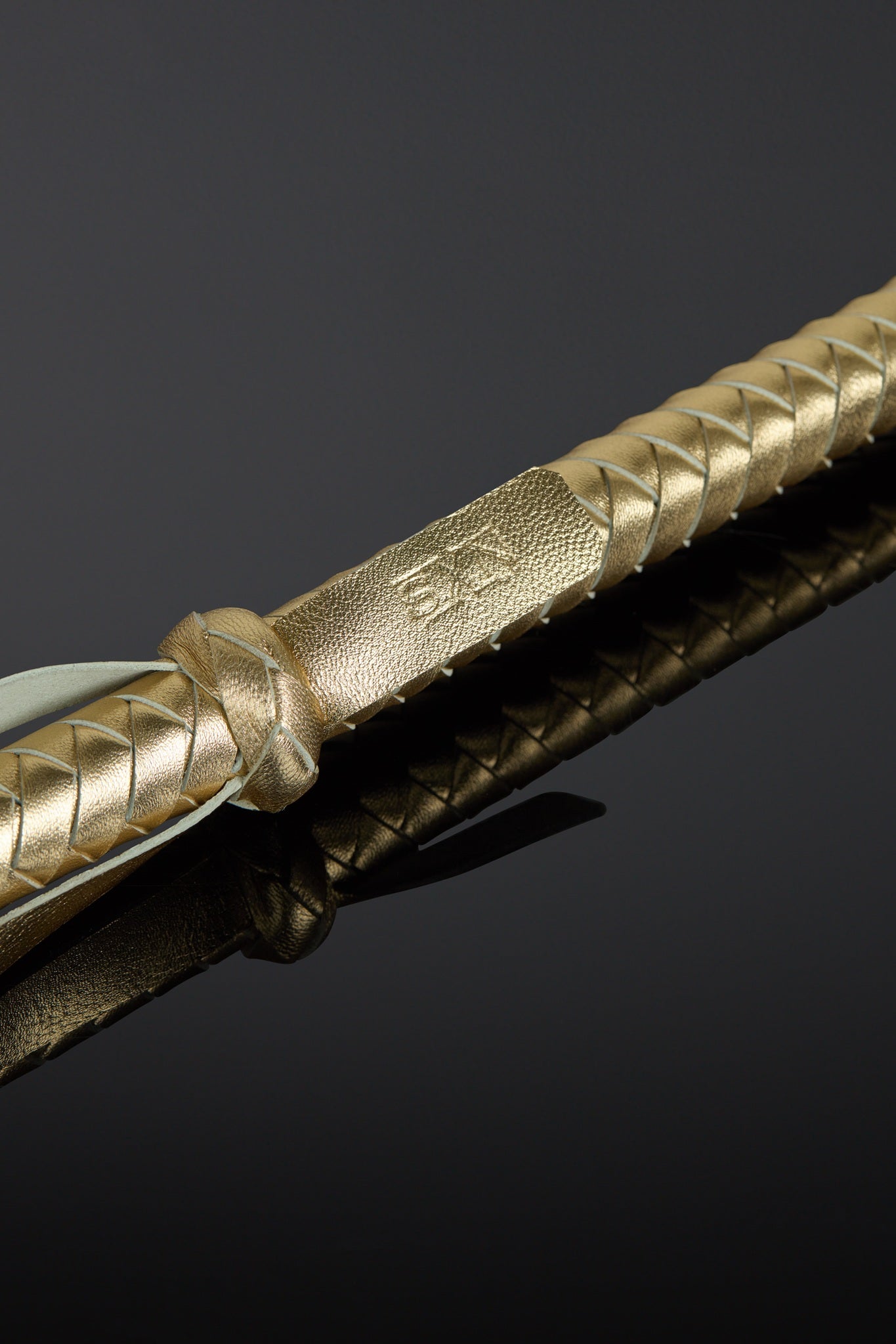 Close-up of a gold-handled leather baton on a black background
