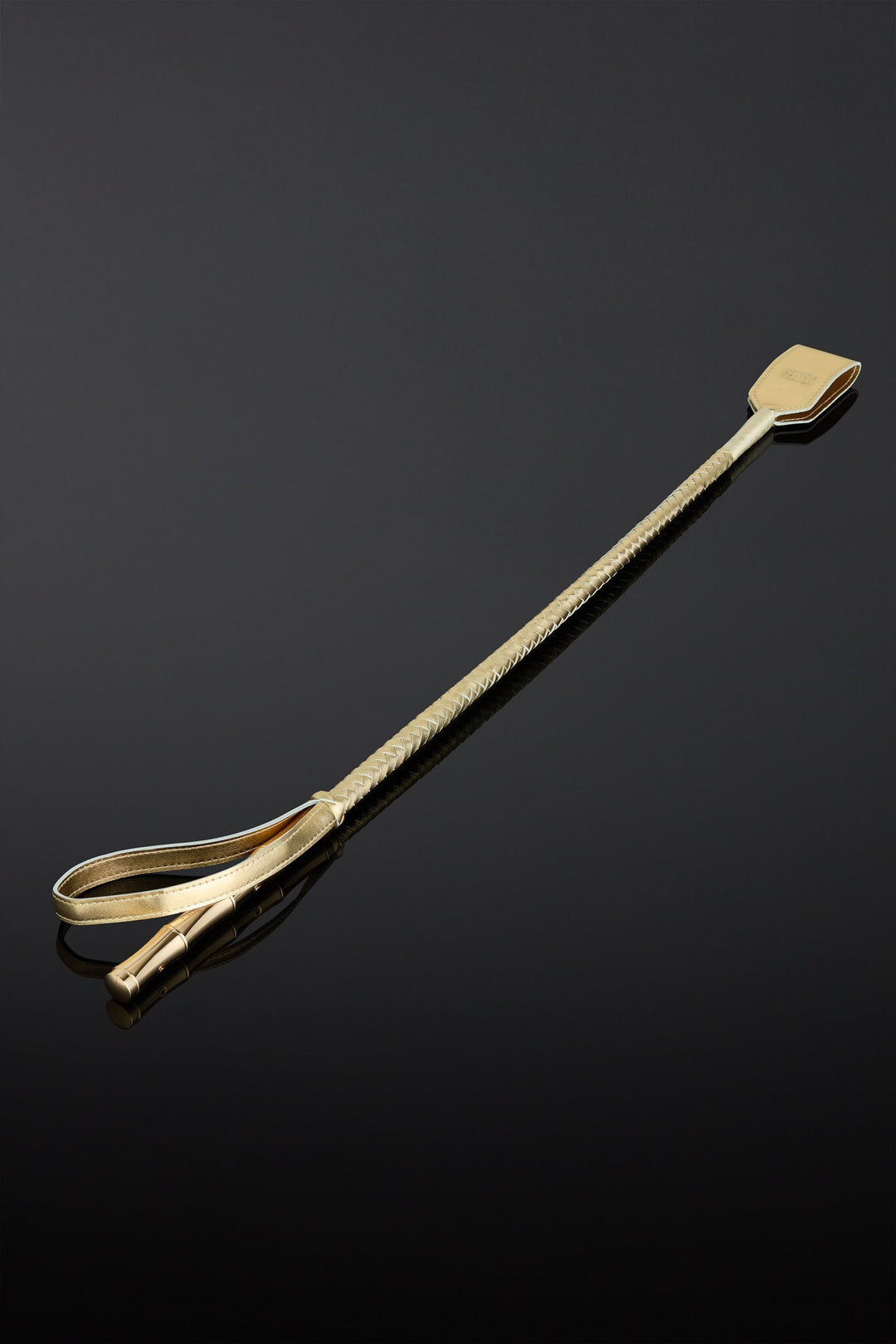 A gold leather crop with metal gold color handle on a black background. 