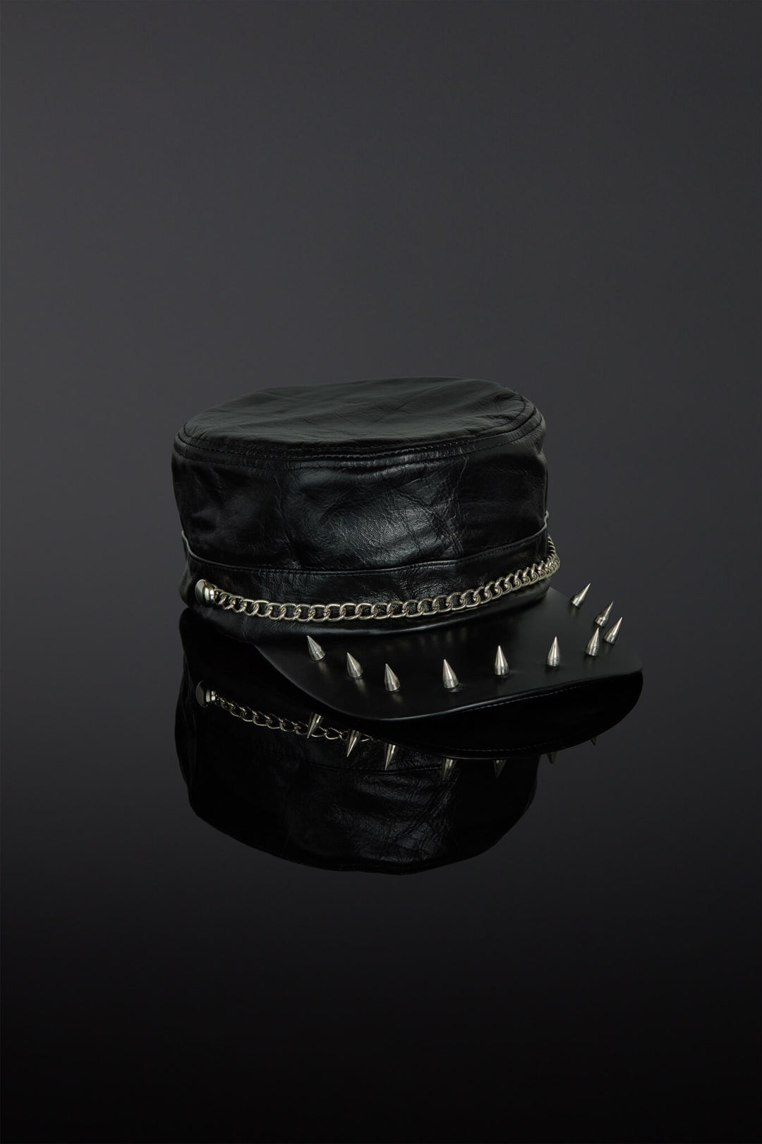 Black leather cap with spikes on a reflective black surface