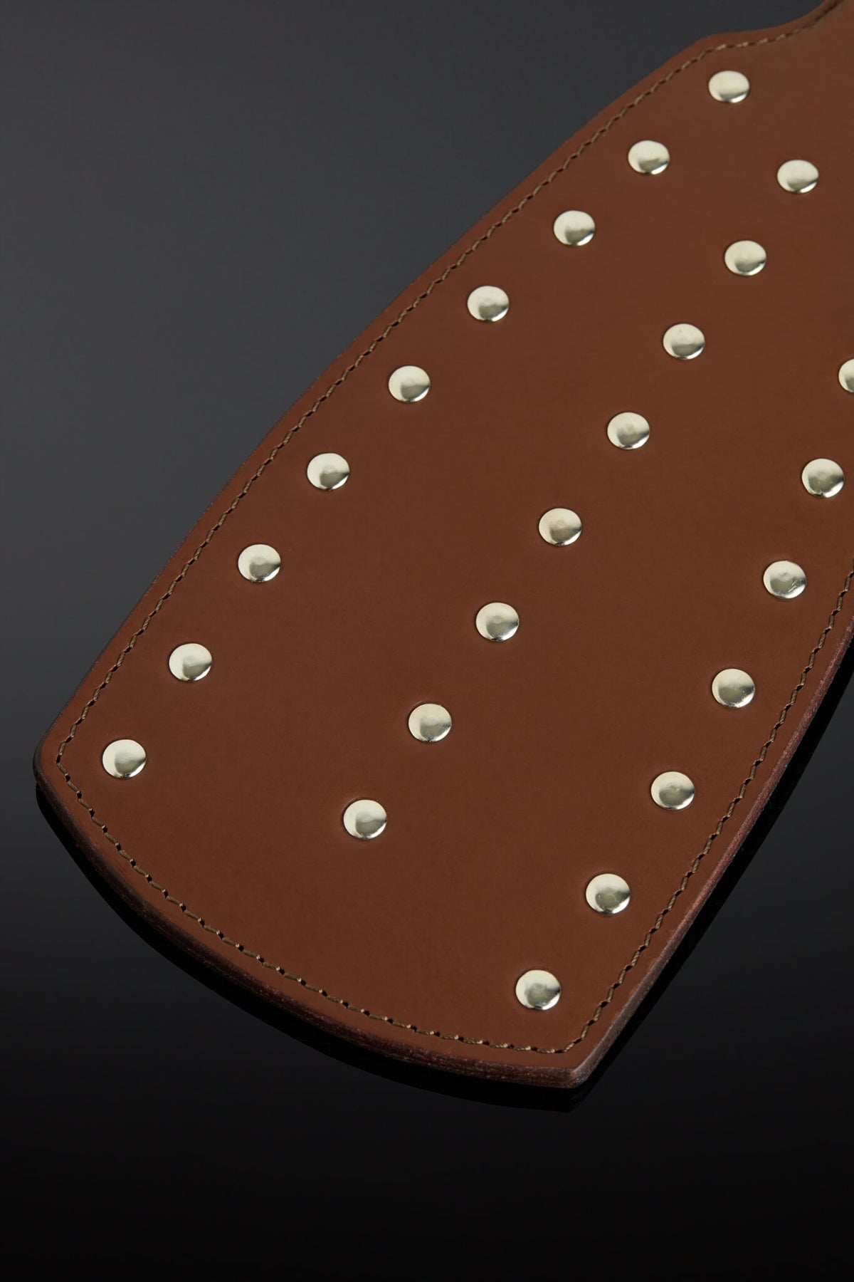 Photo of a brown leather paddle with closeup of the rivets. 