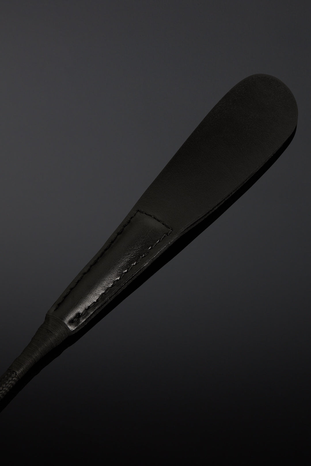 Closeup of black riding crop made from leather on black background