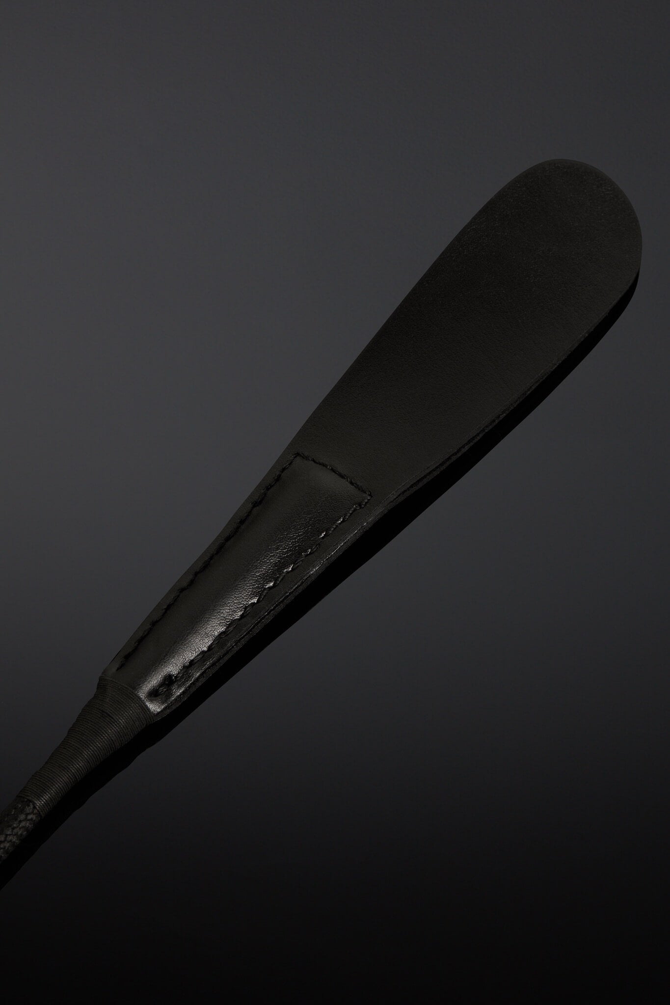 Closeup of black riding crop made from leather on black background