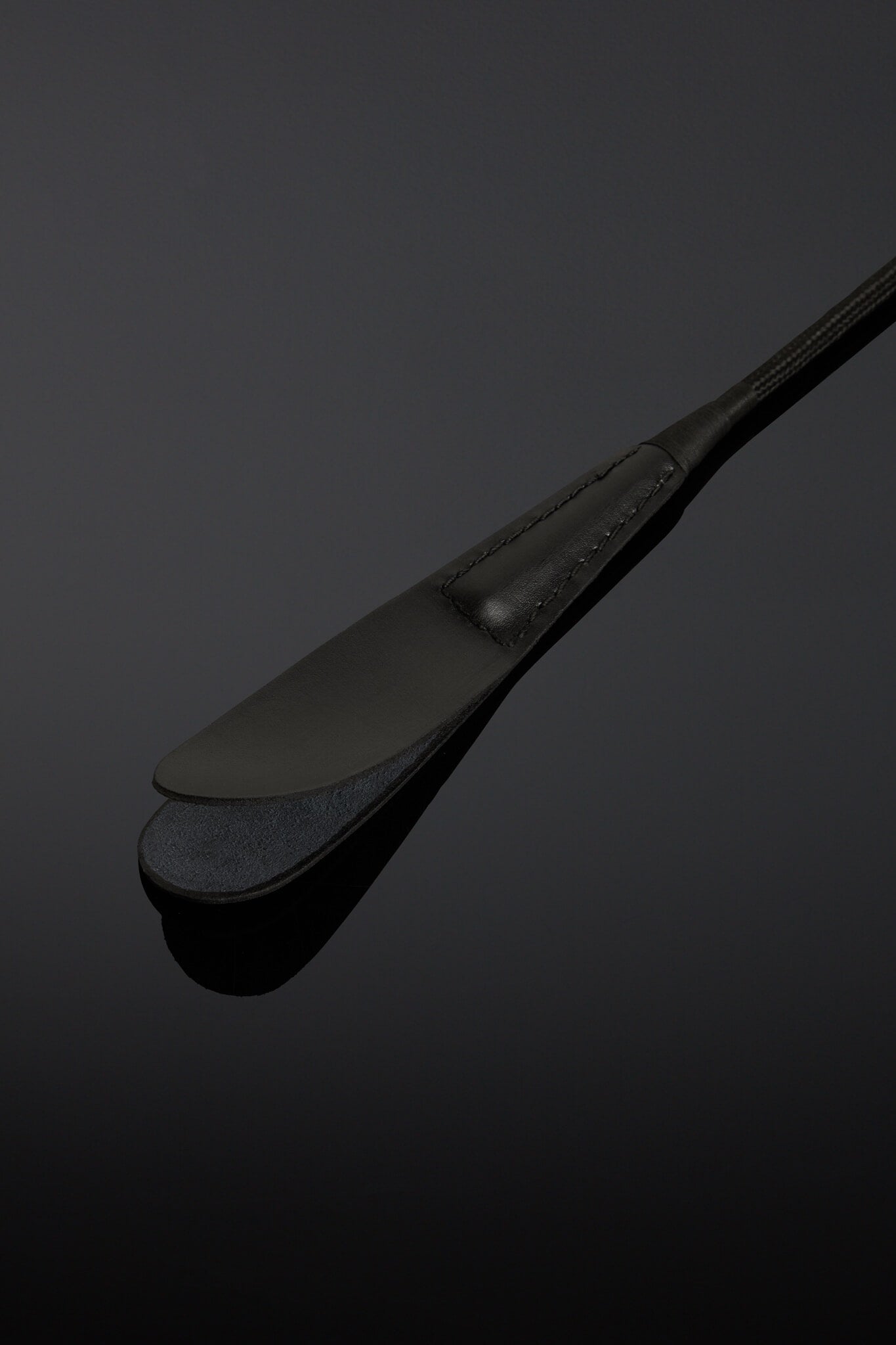closeup of the head of black leather riding crop. On a black background