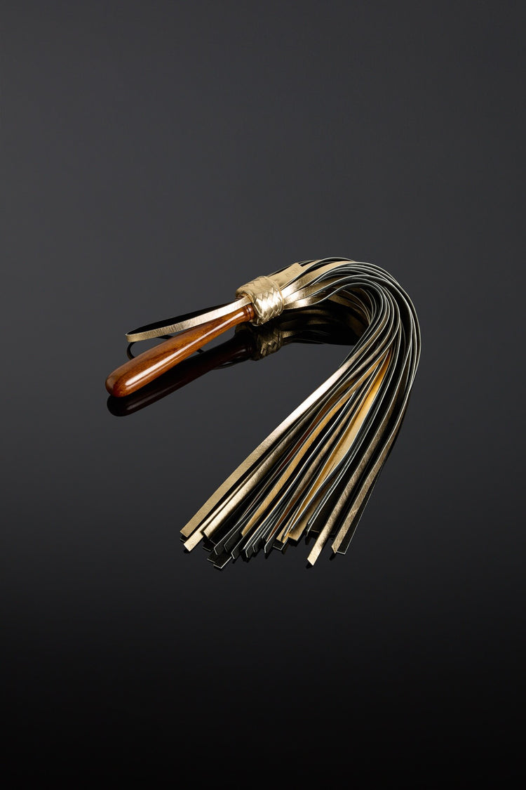 Flogger with wood handle and metallic gold leather tassels on a black background