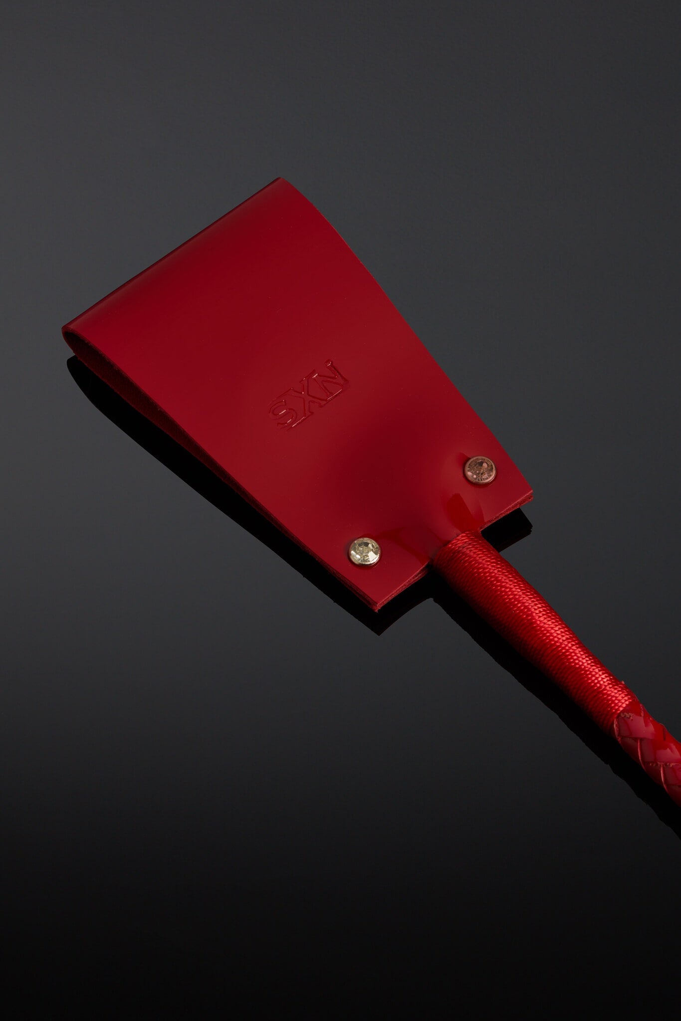 Picture of shiny red leather crop on a black background. 