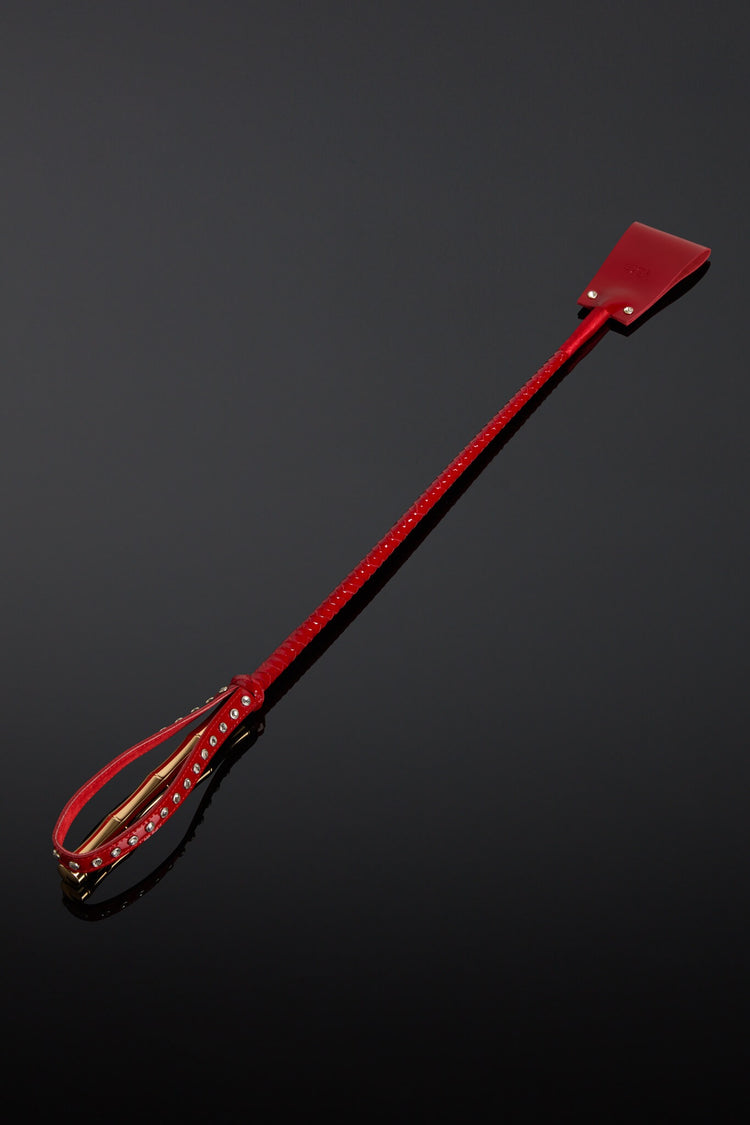 Red leather crop with a gold color  metal handle on a black background