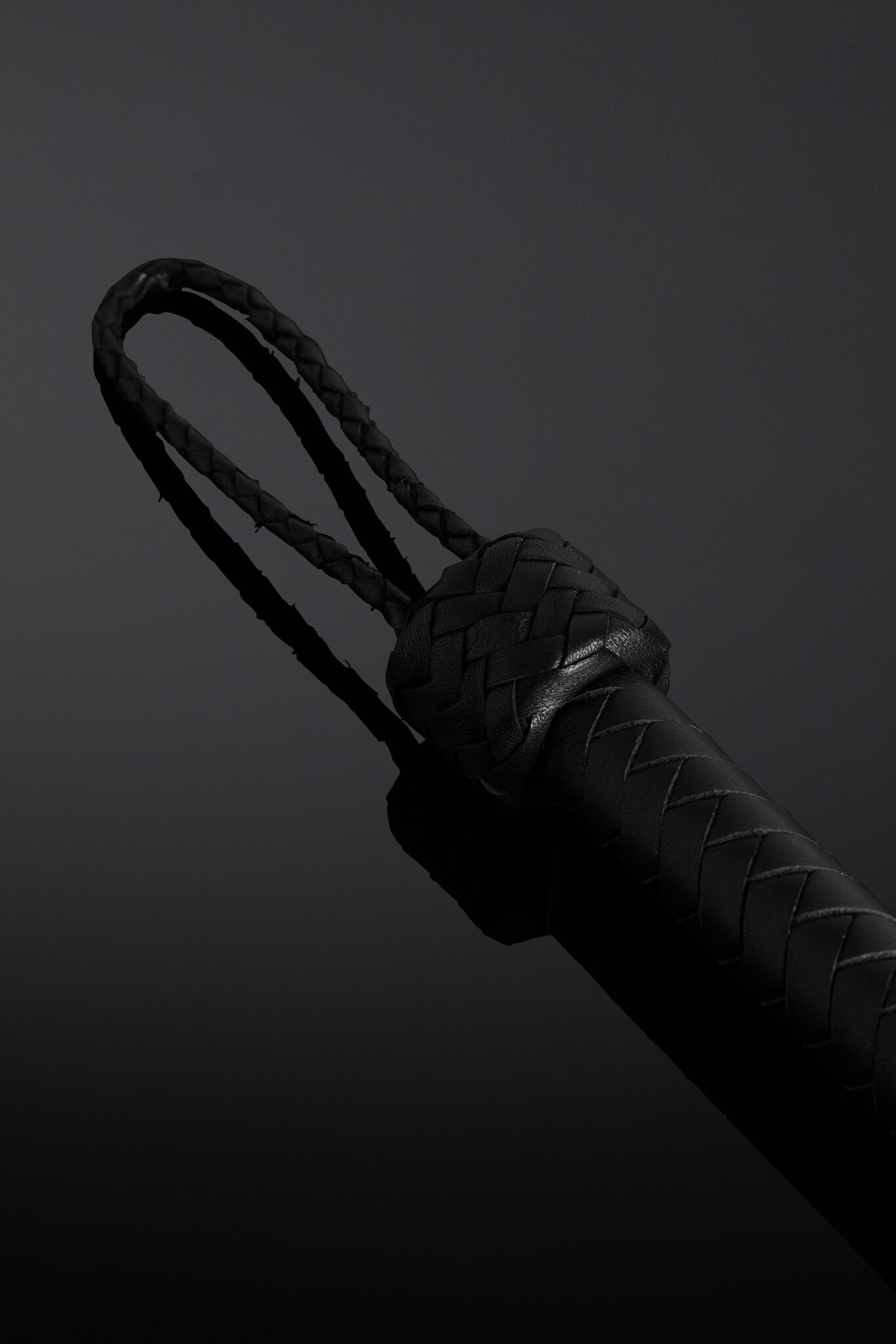 Black barbed wire looking flogger on dark background. Closeup of handle. 