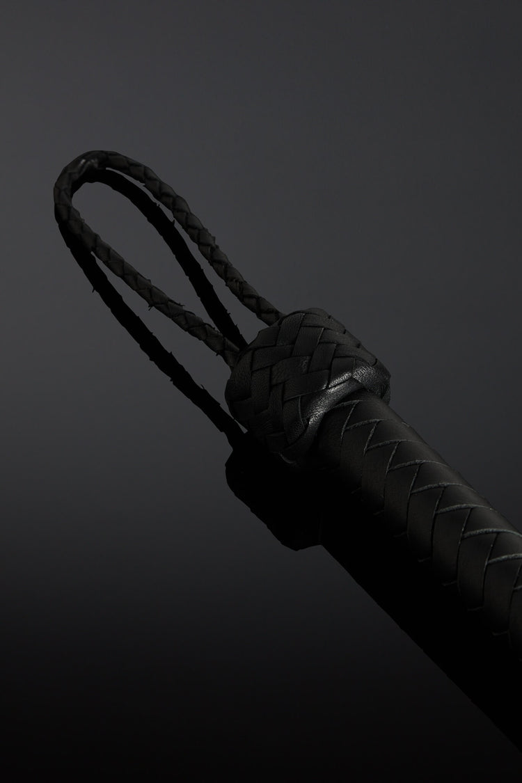 Black barbed wire looking flogger on dark background. Closeup of handle. 