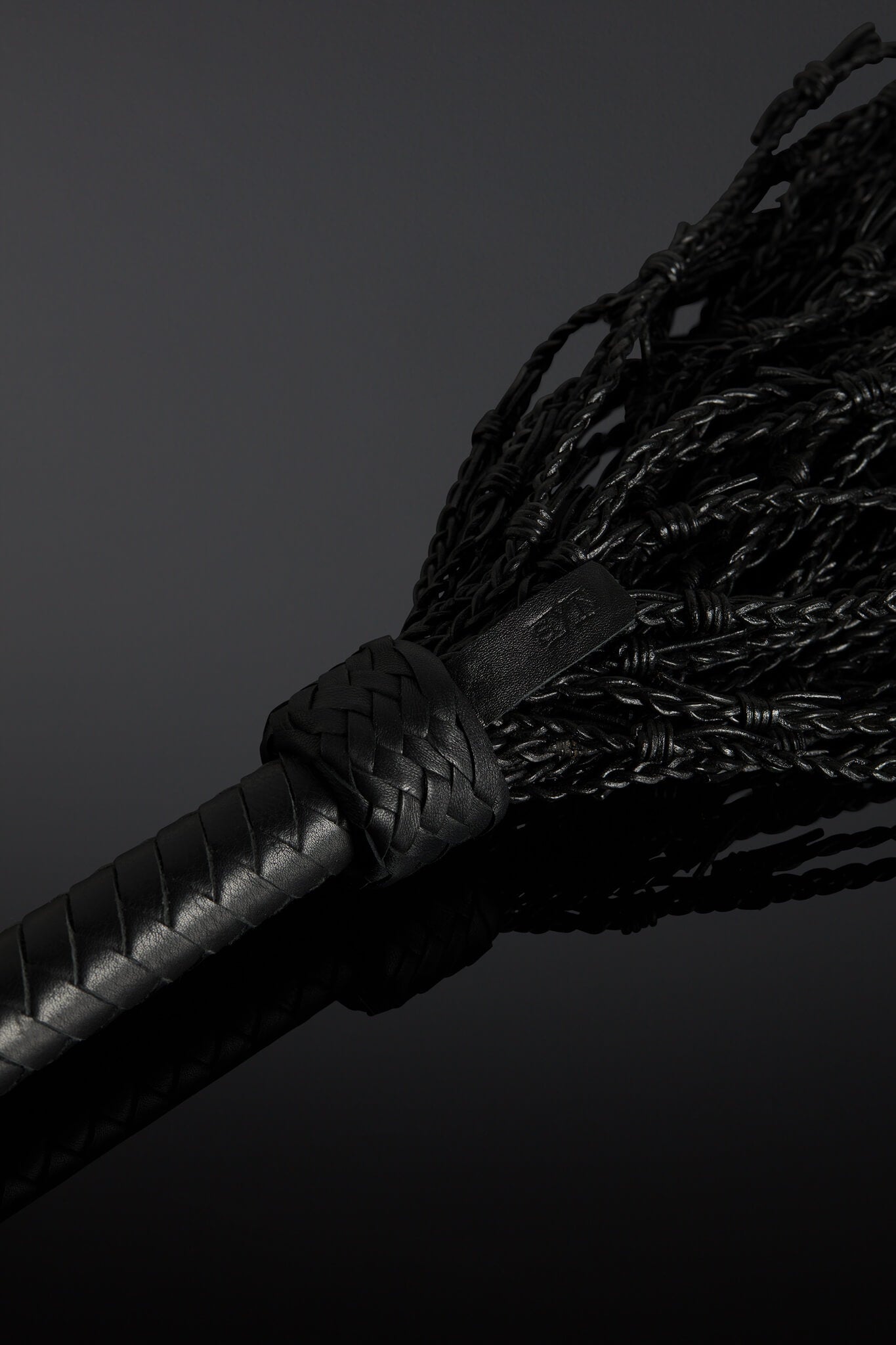 Close-up of a black leather whip with a dark background