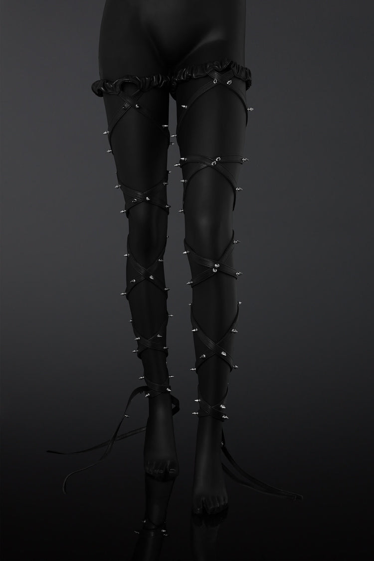 Black leather leg straps with metal spikes designs on a  mannequin legs over a dark background