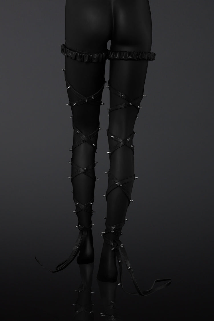 Black leather leg straps with metal spikes designs on a  mannequin legs over a dark background