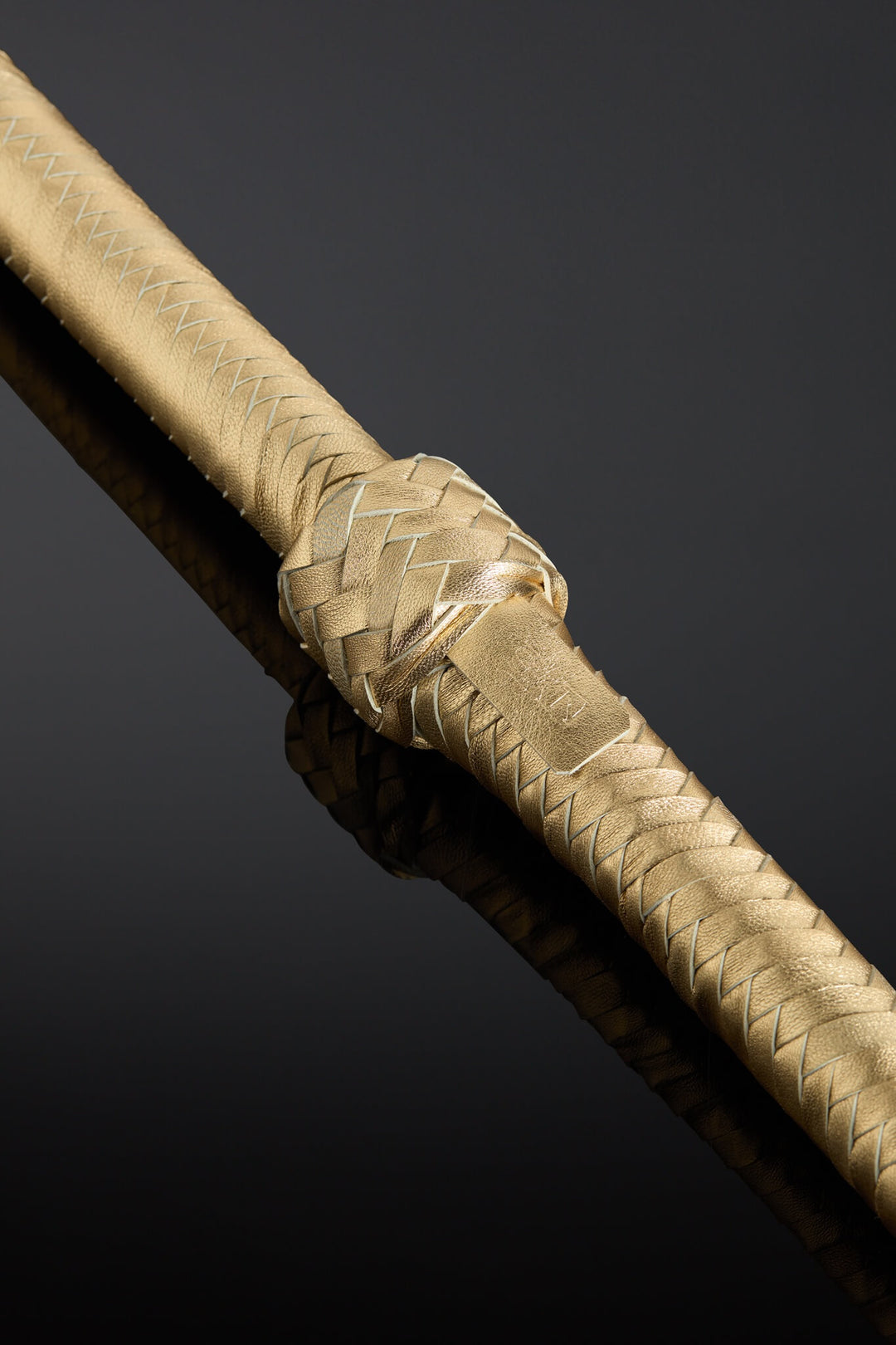 Gold whip handle with an intricate design on a dark background