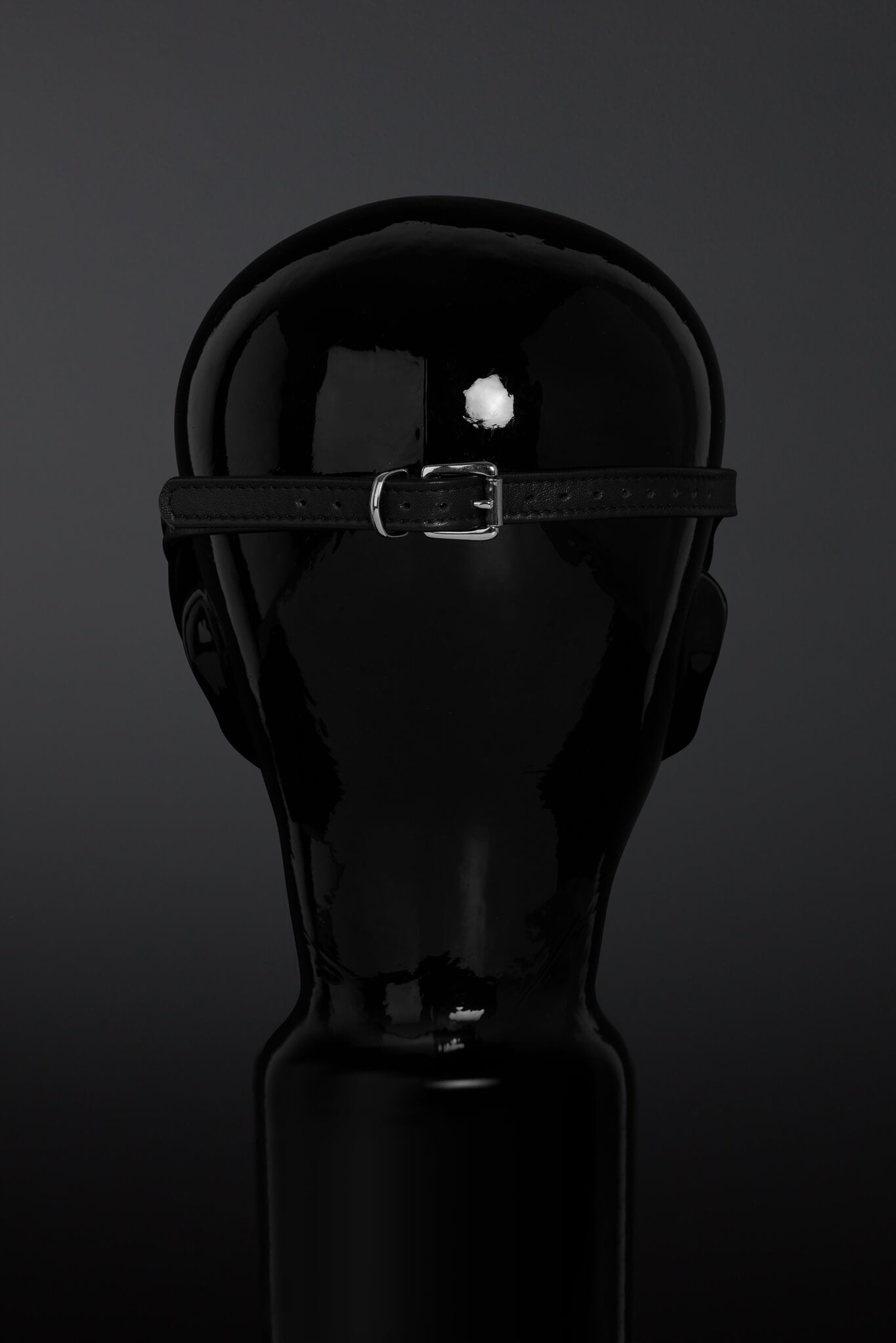 Black leather belt strap and buckle on a mannequin head against a dark background