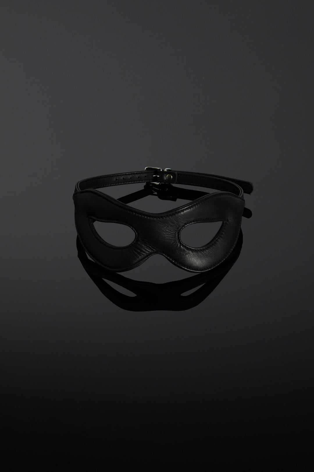 Black leather mask on a reflective black surface with a dark background