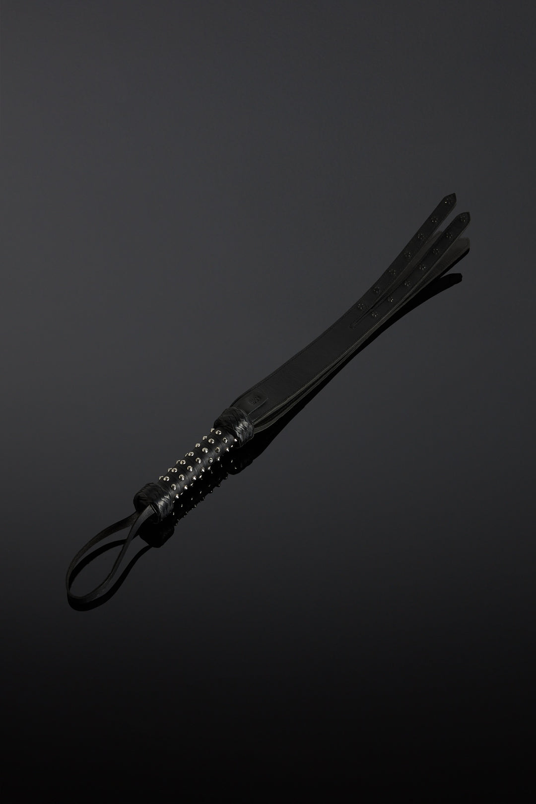 Black leather whip with a metal-adorned handle on a dark background