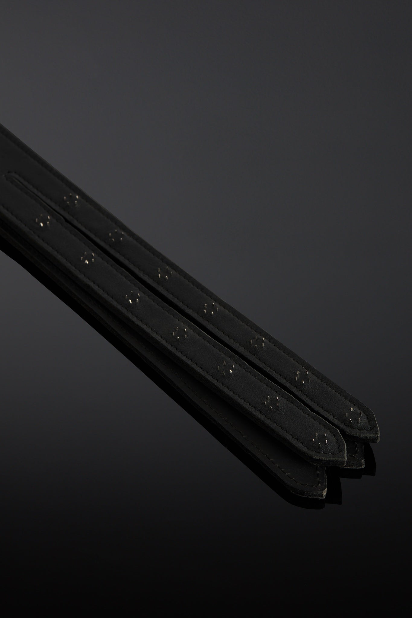 Black leather whip with a metal-adorned handle on a dark background